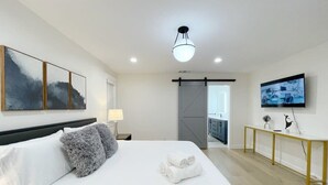 Een moderne slaapkamer met een groot bed, een nachtkastje, een lamp, een televisie en kunstwerken aan de muur.