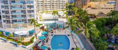 A hotel with a rooftop swimming pool, surrounded by palm trees and a landscaped garden.