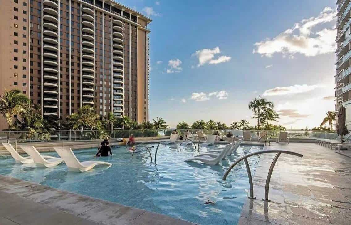 A swimming pool area with lounge chairs and a tall building in the background.