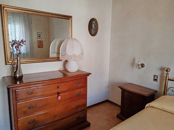 Ein Schlafzimmer mit einem hölzernen Schminktisch, einem Nachttisch, einer Lampe, einem Bett, einem Spiegel und einer Wandleuchte.