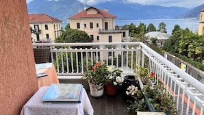 Een balkon met uitzicht op zee en bergen, rieten meubilair en potplanten.