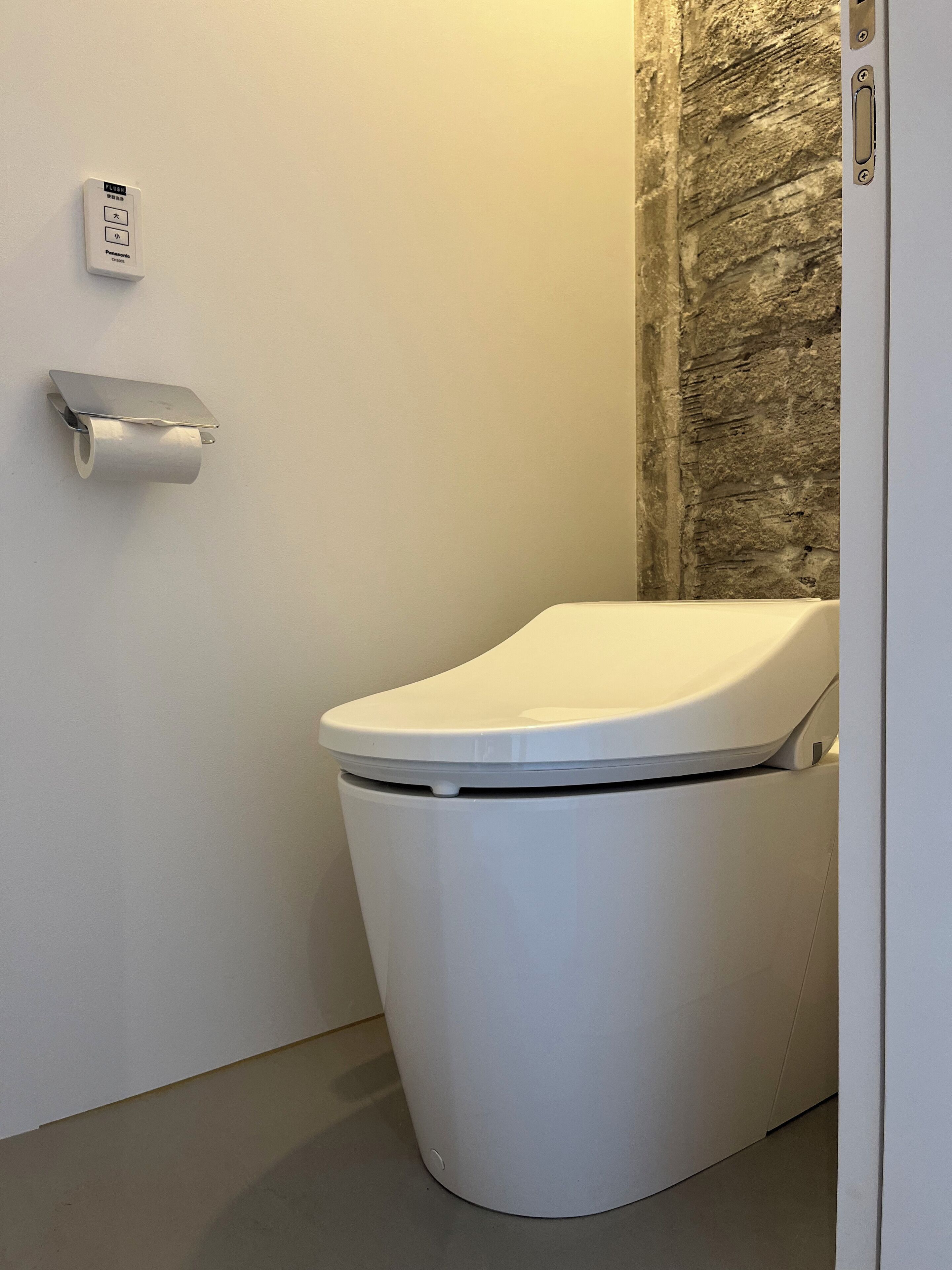 A modern toilet with a flush handle and a toilet paper holder on the wall.