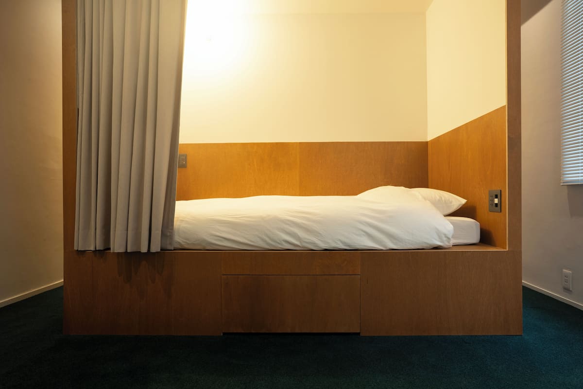 Uma cama de solteiro com cabeceira de madeira num quarto de canto.