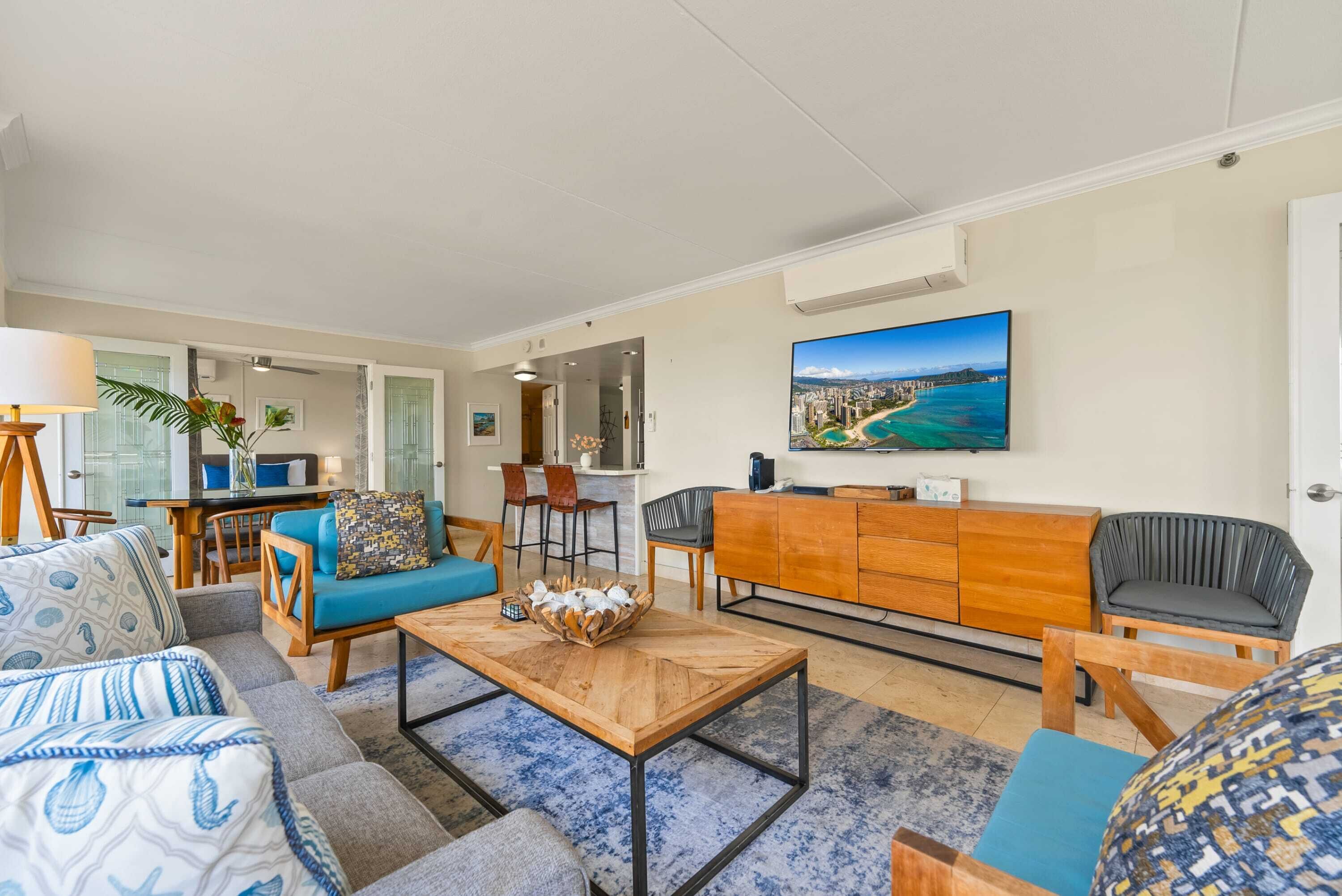 A modern living room with a sofa, armchairs, a coffee table, and a TV mounted on the wall.