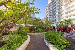 A pathway flanked by lush greenery and a tall building with balconies. - @ Marbella Lane - Cozy 2BR w/ Amazing Ocean Views (Honolulu)