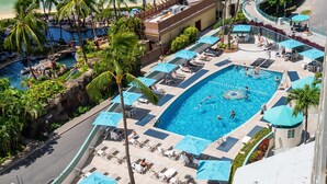 Una gran piscina al aire libre rodeada de sillas de descanso y sombrillas, con palmeras y un edificio al fondo.