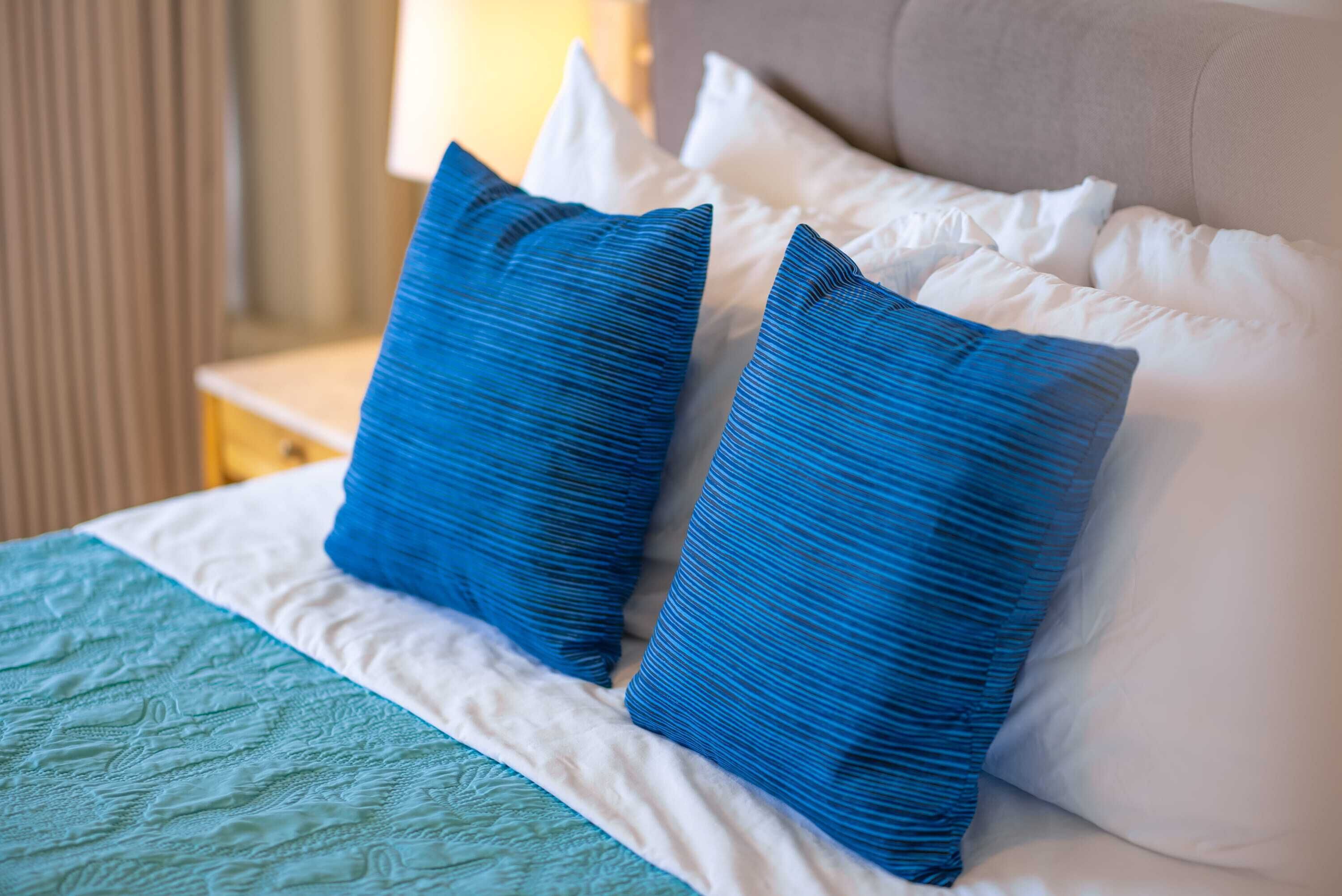A bed with a teal quilt and two blue pillows.