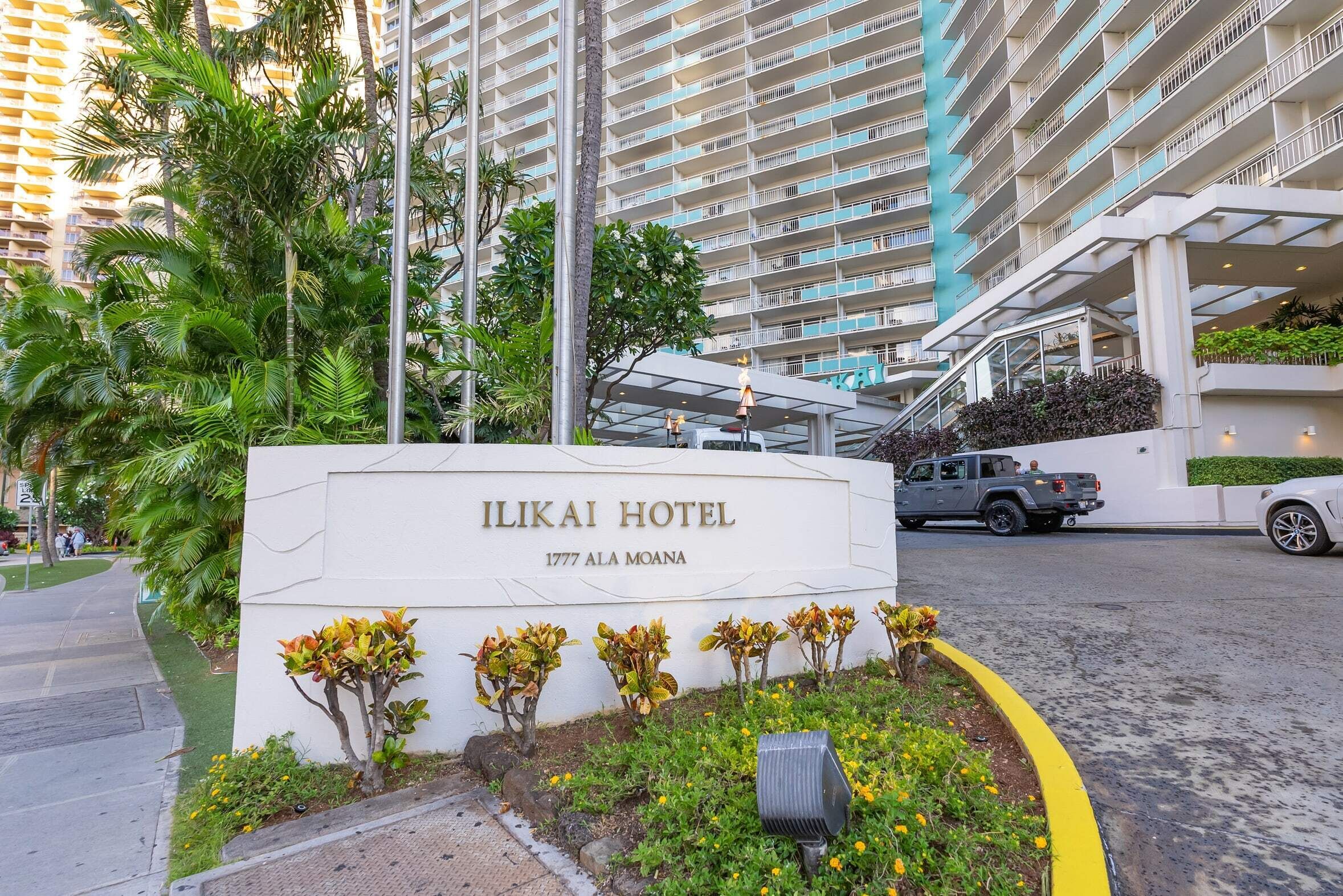 Exterior del Hotel Ilikai con un letrero, un estacionamiento y un edificio alto al fondo.