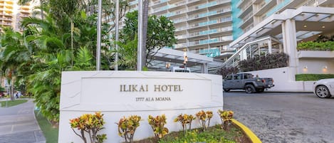 Exterior del Hotel Ilikai con un letrero, un estacionamiento y un edificio alto al fondo.