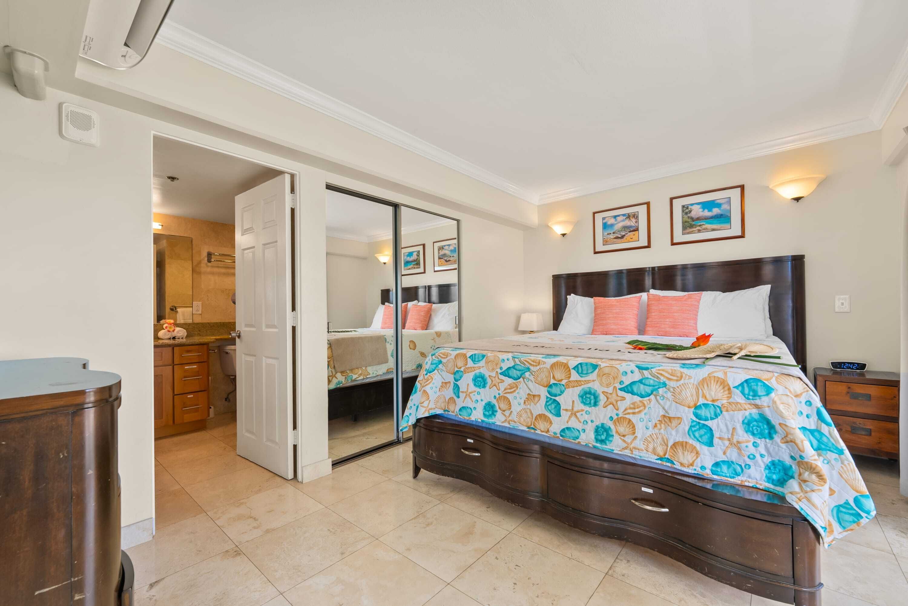 A bedroom with a bed, a nightstand, a dresser, a mirror, and a door leading to a bathroom.