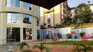 Un bâtiment à la façade incurvée, doté de grandes fenêtres et d’une aire de jeux avec des balançoires et des toboggans.