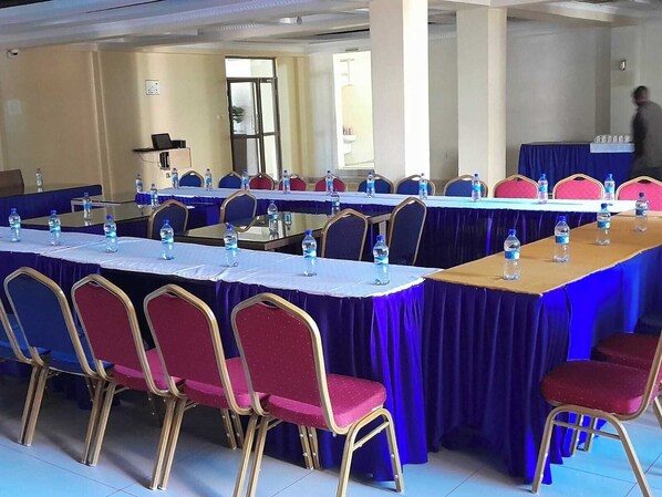 A conference room with multiple tables and chairs, water bottles on each table, and a person walking in the background. - The Village Park Resort & Spa (Keumbu)