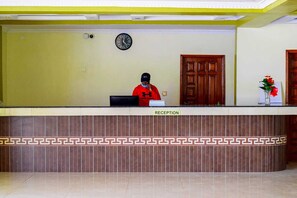 A reception desk with a clock, a wooden door, and a vase with flowers. - The Village Park Resort & Spa (Keumbu)