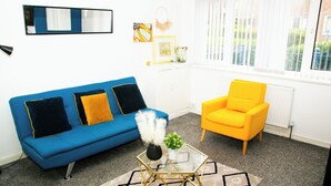 Ein Wohnzimmer mit einem blauen Sofa, einem gelben Sessel und einem Glastisch mit Dekoration.