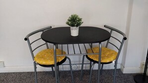 Ein runder Tisch mit zwei Stühlen, jeder mit einem gelben Kissen. Auf dem Tisch steht ein kleiner Blumentopf.