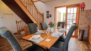 A dining area with a wooden table set for four, surrounded by upholstered chairs. A staircase with wooden railings is visible in the background. - 2loos (Newton Stewart)
