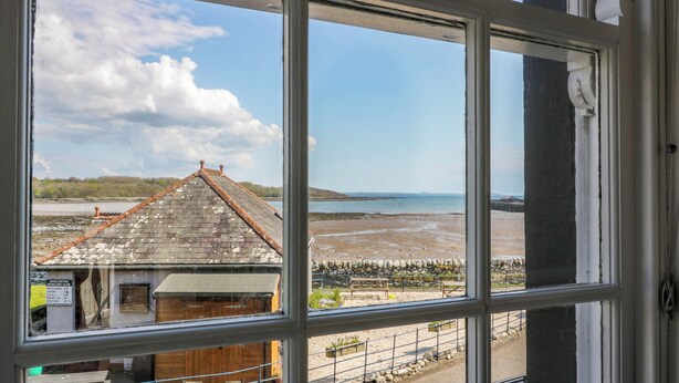 A view through a window of a coastal building with a tiled roof, a sandy beach, and a clear sky. - 2loos (Newton Stewart)