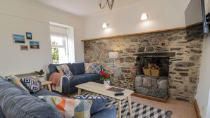A living room with a stone fireplace, a blue sofa set, and a patterned rug. - 2loos (Newton Stewart)