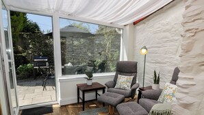 A cozy room with a large window, a comfortable seating area with a chair and a sofa, a small table, and a potted plant. - 2loos (Newton Stewart)