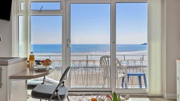 A balcony with a view of the beach, a dining table with chairs, and a TV mounted on the wall. - 9 Strandways - Sea Views, Parking, Beach Access (Saundersfoot)