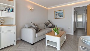 A modern living room with a sofa, a coffee table, and a bookshelf. - 9 Strandways - Sea Views, Parking, Beach Access (Saundersfoot)