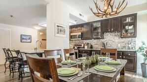 Una cocina moderna con armarios de madera oscura, encimera de granito y comedor con mesa de vidrio para seis personas.
