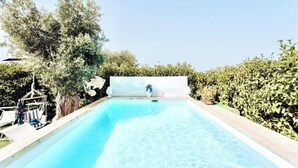 Una piscina con agua cristalina azul, rodeada de follaje y un muro blanco.