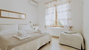 Un dormitorio con una cama grande, un sofá más pequeño, una ventana con cortinas traslúcidas y un radiador.