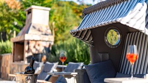 A cozy outdoor seating area with a stone fireplace, lounge chairs, and a table with a glass of red wine. - Gorgeous home in Ehrenhausen (Ehrenhausen)