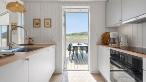 A kitchen with white cabinets, a wooden countertop, a sink, a hanging light, and a view of a deck with chairs. - Lovely home in Stege with sauna (Stege)