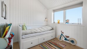 A bedroom with a white bed, a window with a view, a toy bicycle, and a colorful rug. - Lovely home in Stege with sauna (Stege)