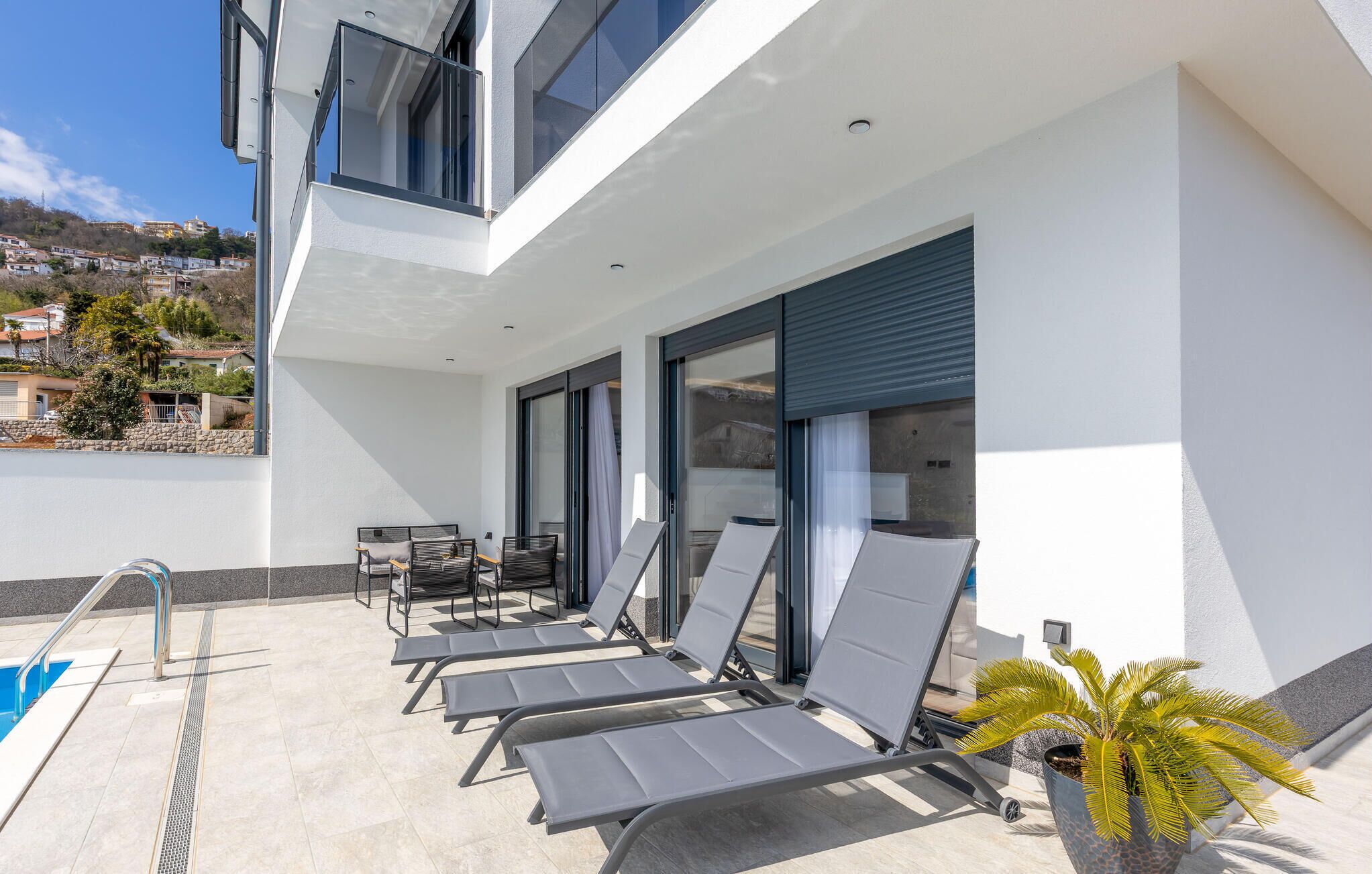 Un espace extérieur moderne doté d’une piscine, de chaises longues et d’une plante en pot.