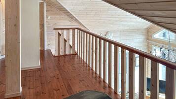 A wooden interior with a staircase leading to an upper level, a bench, and a visible outdoor area with a view.