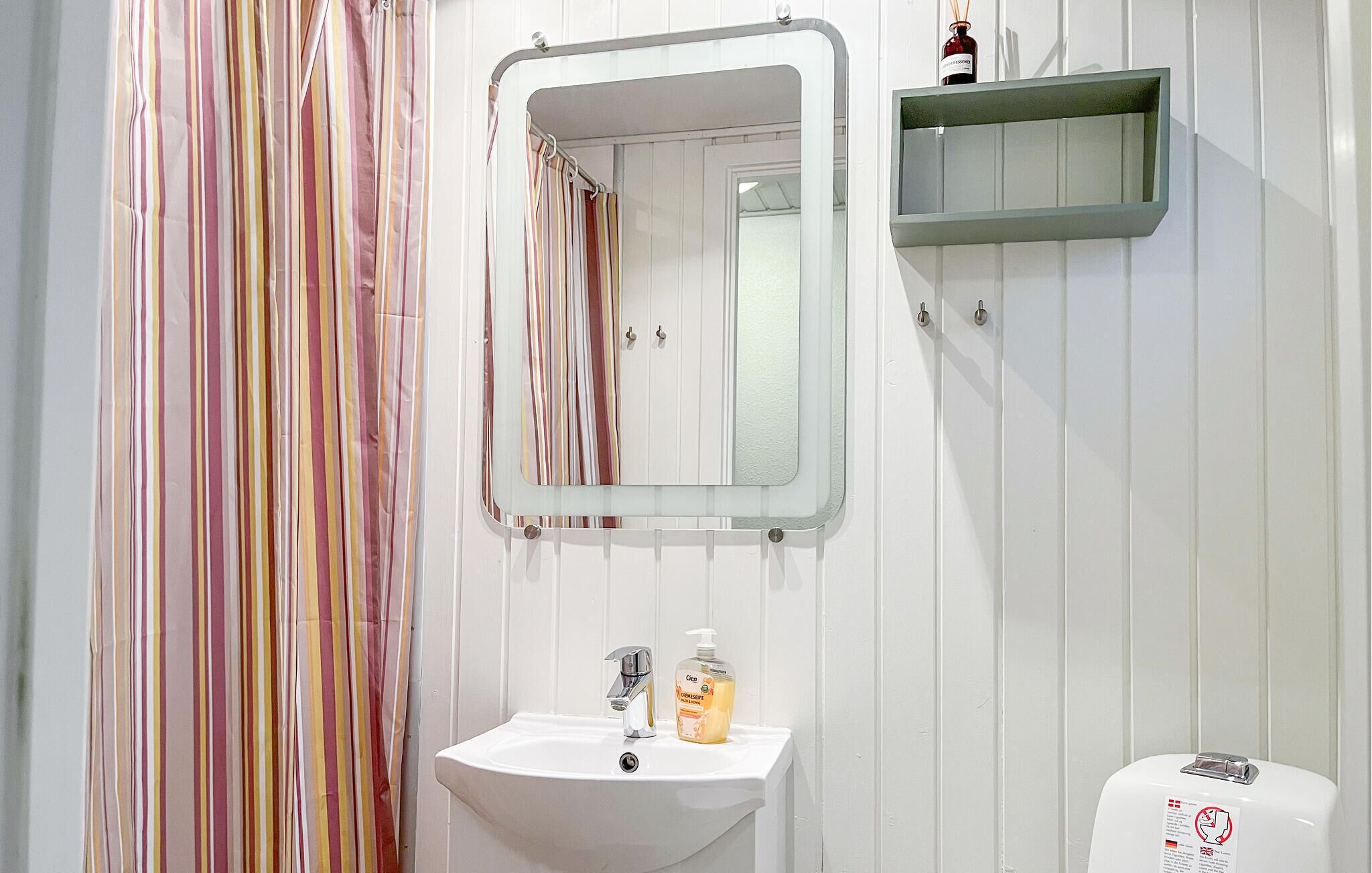 Une salle de bain avec un lavabo blanc, un miroir, un rideau de douche à rayures et un distributeur de savon.