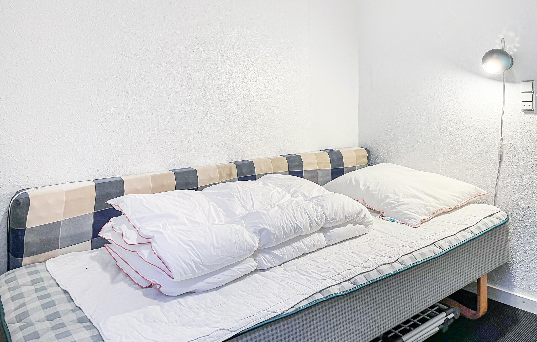 A bed with a checkered headboard, white bedding, and a bedside lamp.