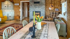 Ein gemütliches Wohnzimmer mit Kamin, Holzwänden, einem Esstisch mit einer Vase voller Tulpen und einer Gitarre an der Wand.