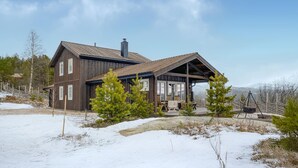 Eine zweistöckige Holzhütte mit überdachter Veranda, umgeben von verschneitem Boden und spärlicher Vegetation.