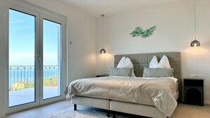 A bedroom with a large bed, two bedside tables, a wall-mounted light fixture, and a view through a sliding door.
