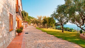 A stone-paved pathway leading to a building with a stone facade and wooden shutters.