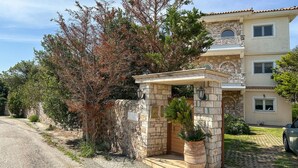 Un bâtiment à deux étages avec une façade en pierre, une entrée couverte avec des marches et une voiture garée devant.