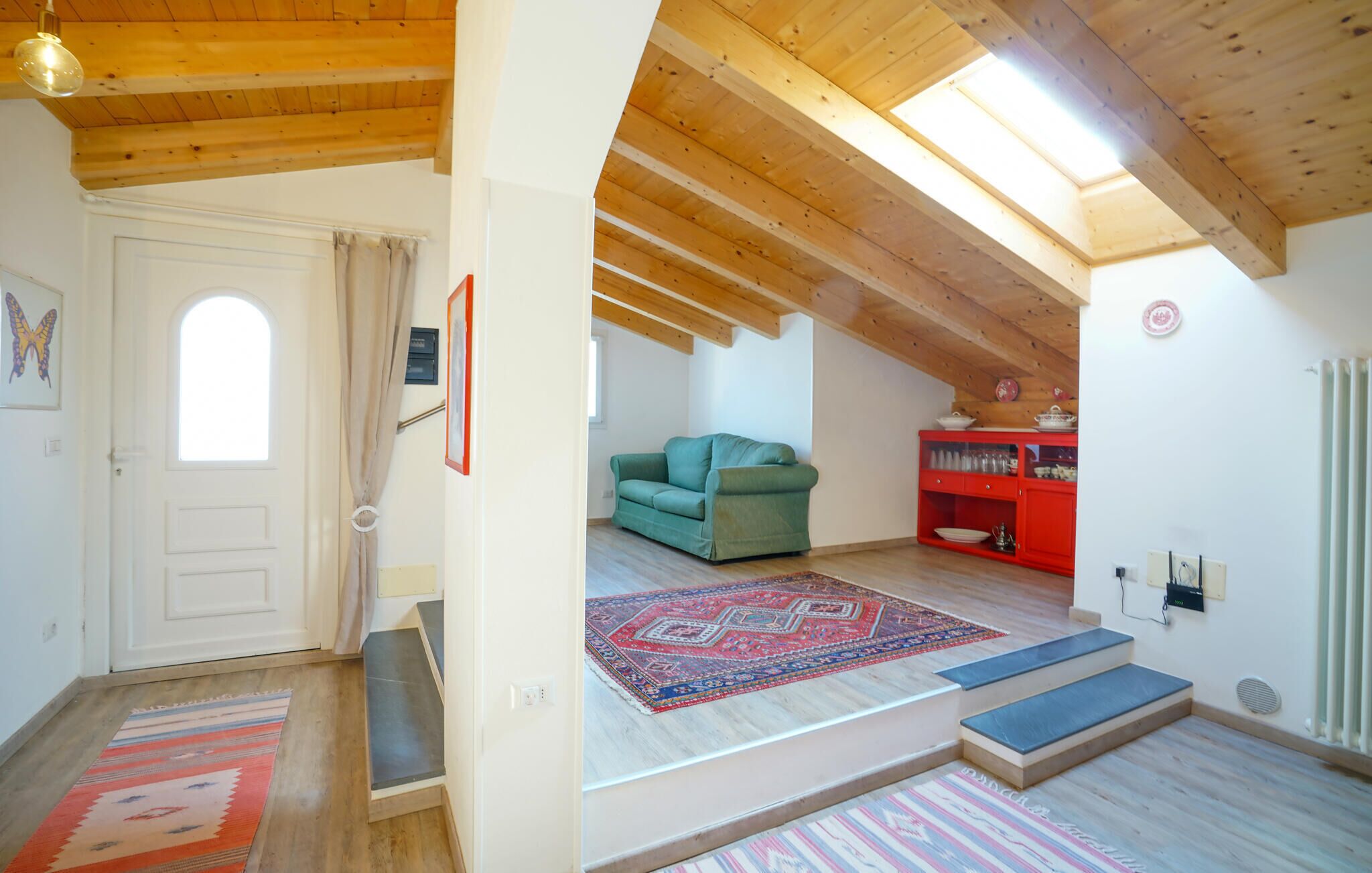 A loft-style room with a wooden ceiling, a green sofa, a red cabinet, and a patterned rug.