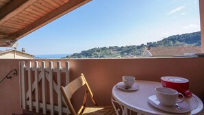 A balcony with a wooden ceiling, a wicker chair, a white table with two cups and a red cup, and a view of a hilly landscape. - Lovely home in Imperia with WiFi (Imperia)