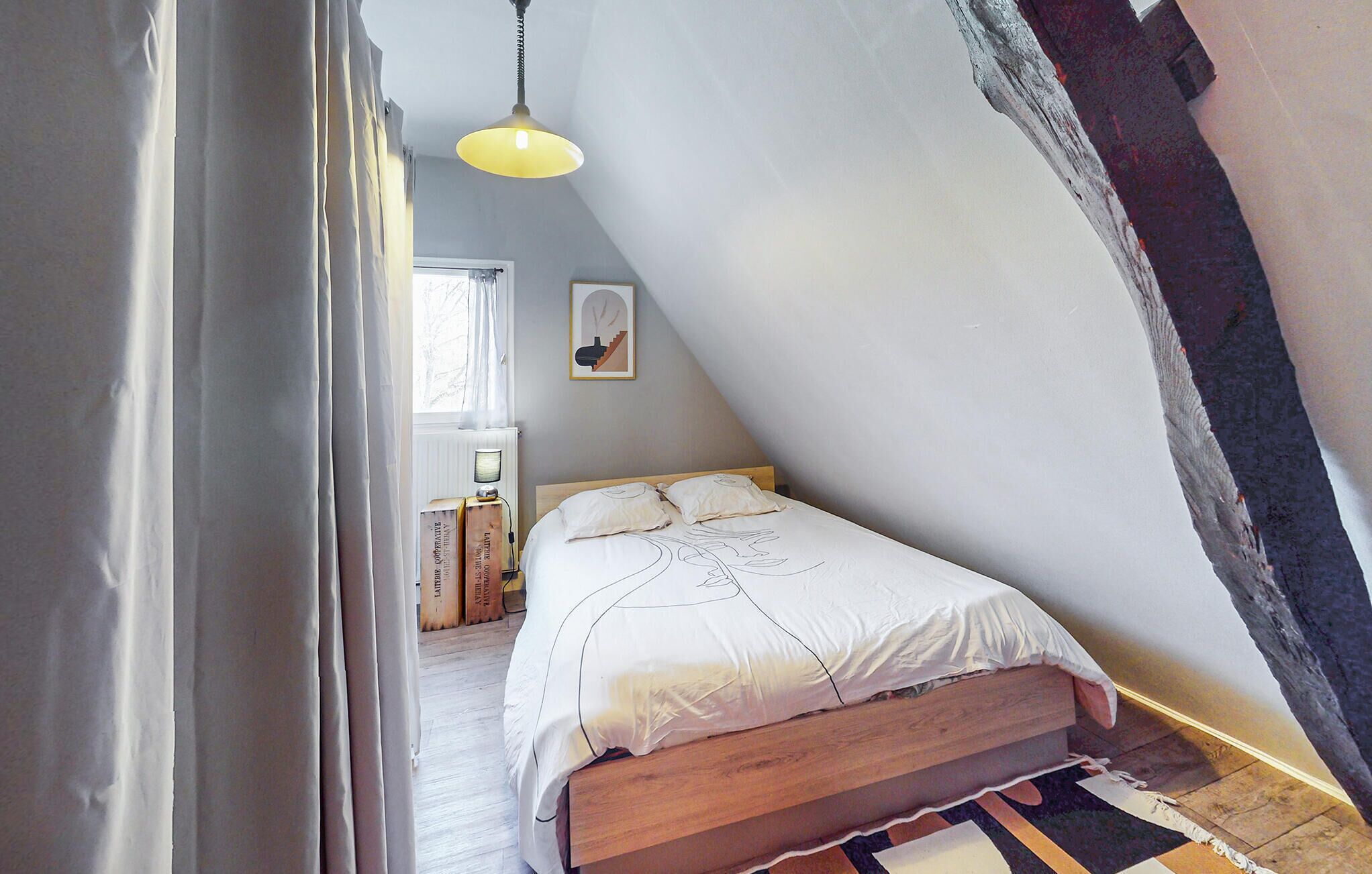 Quarto com teto inclinado, estrutura de cama de madeira e colcha branca.