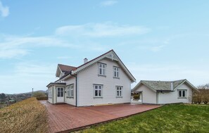 Une maison à deux étages avec une terrasse en bois et un petit garage attenant.