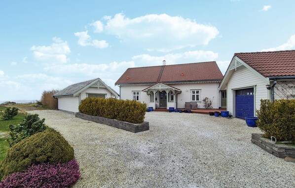 Une maison à deux étages avec une allée en gravier, un porche à l’avant et un garage.