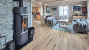 A cozy living room with a stone wall, a fireplace, and a kitchen in the background. - Awesome home in Bekkjarvik (Bekkjarvik)