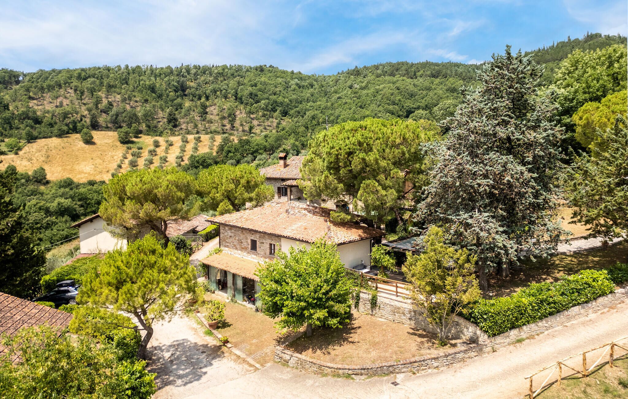 A rural house with a stone facade, surrounded by trees and a hilly landscape.
