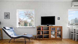 Un soggiorno con una poltrona reclinabile, una televisione su un mobile in legno, una libreria e una finestra vista alberi.
