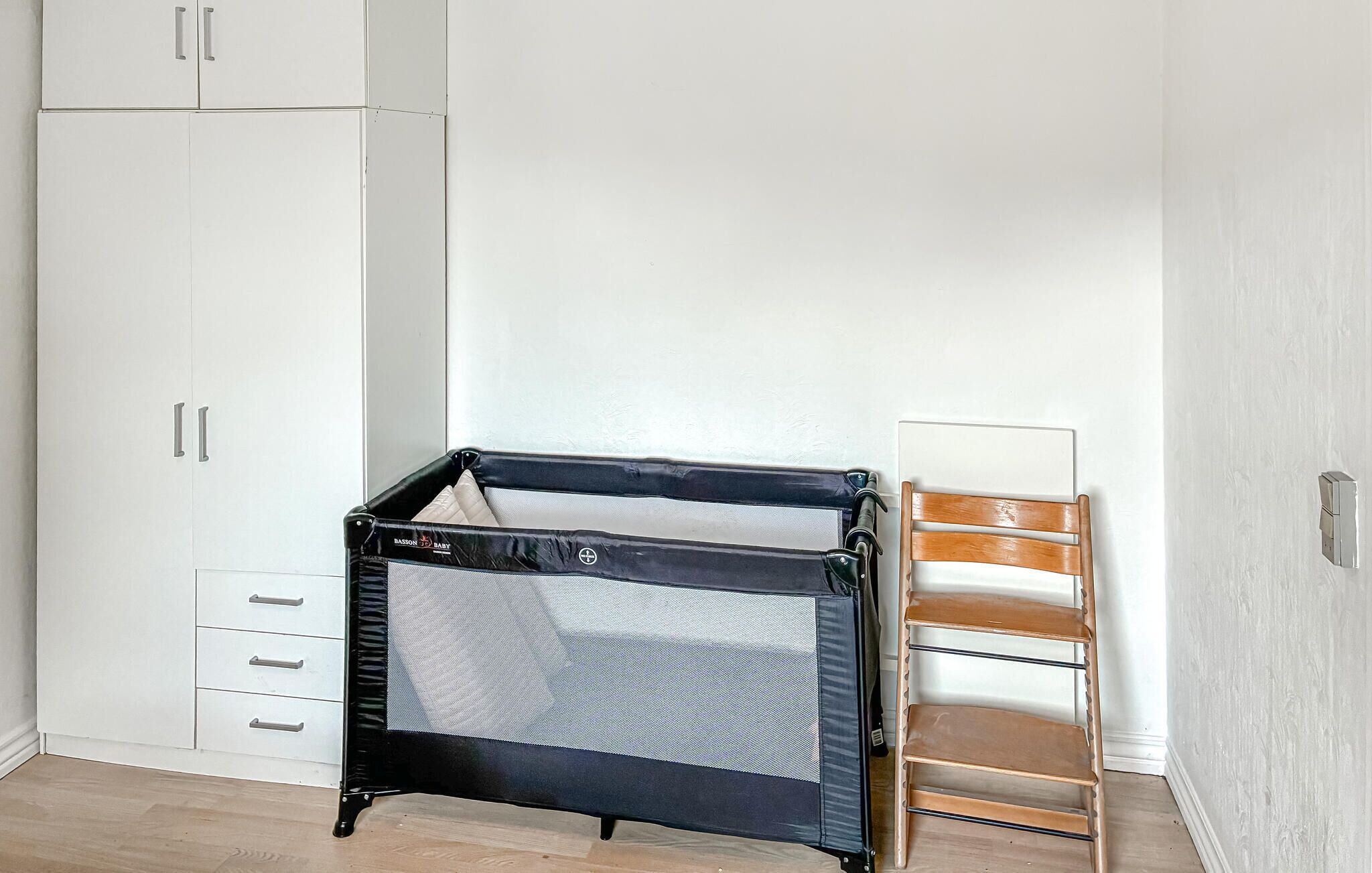 Una habitación con un armario blanco, una cuna pequeña negra y una silla de madera.