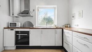 Una cucina compatta con mobili bianchi, un forno a microonde, una lavastoviglie e una finestra vista alberi.